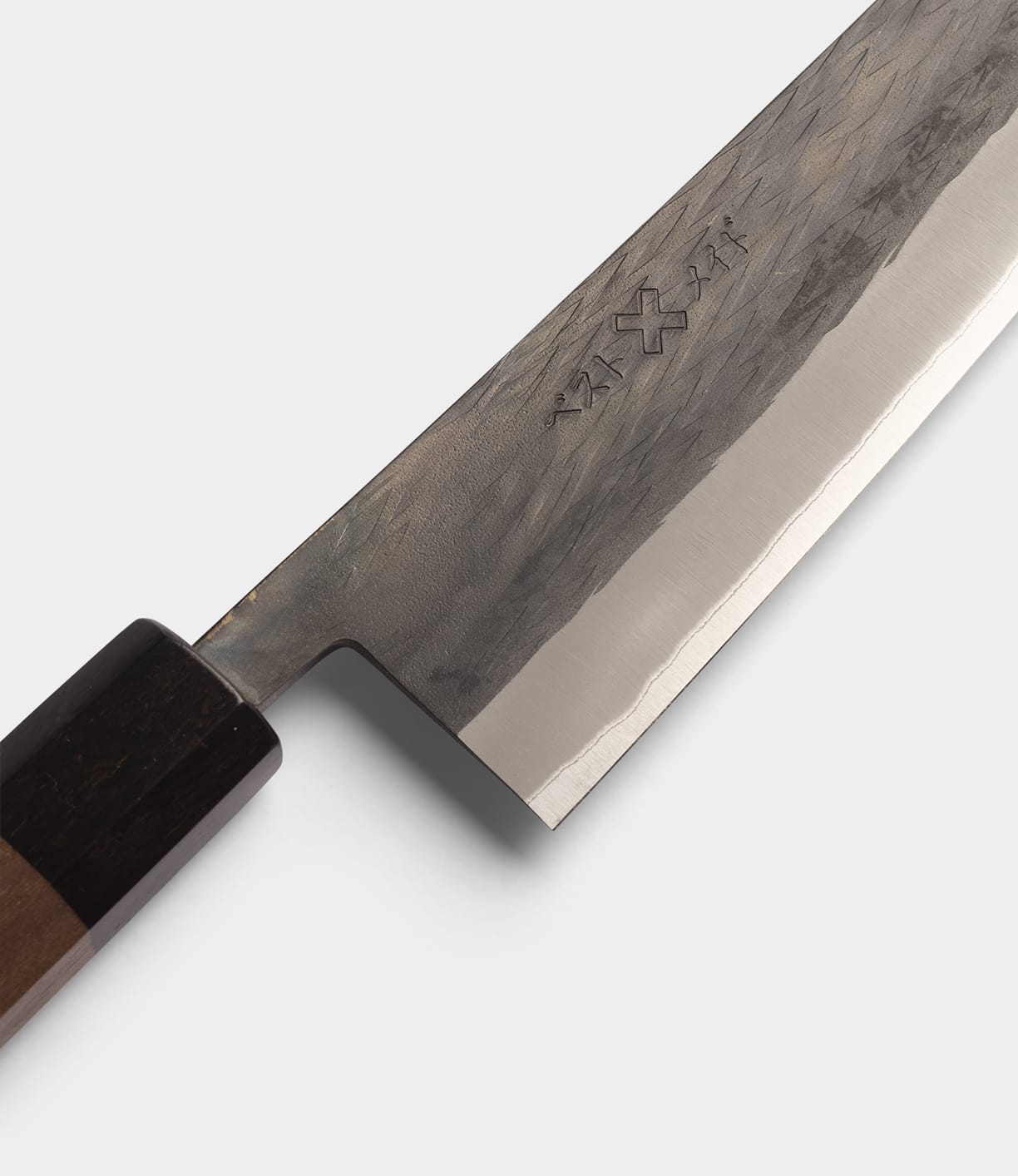 A close-up of the Best Made Co. Aogami Gyuto Knife, featuring a blade crafted from Blue Paper Steel No. 2 with engraved kanji characters and a hammered finish, complemented by a dark wooden handle.