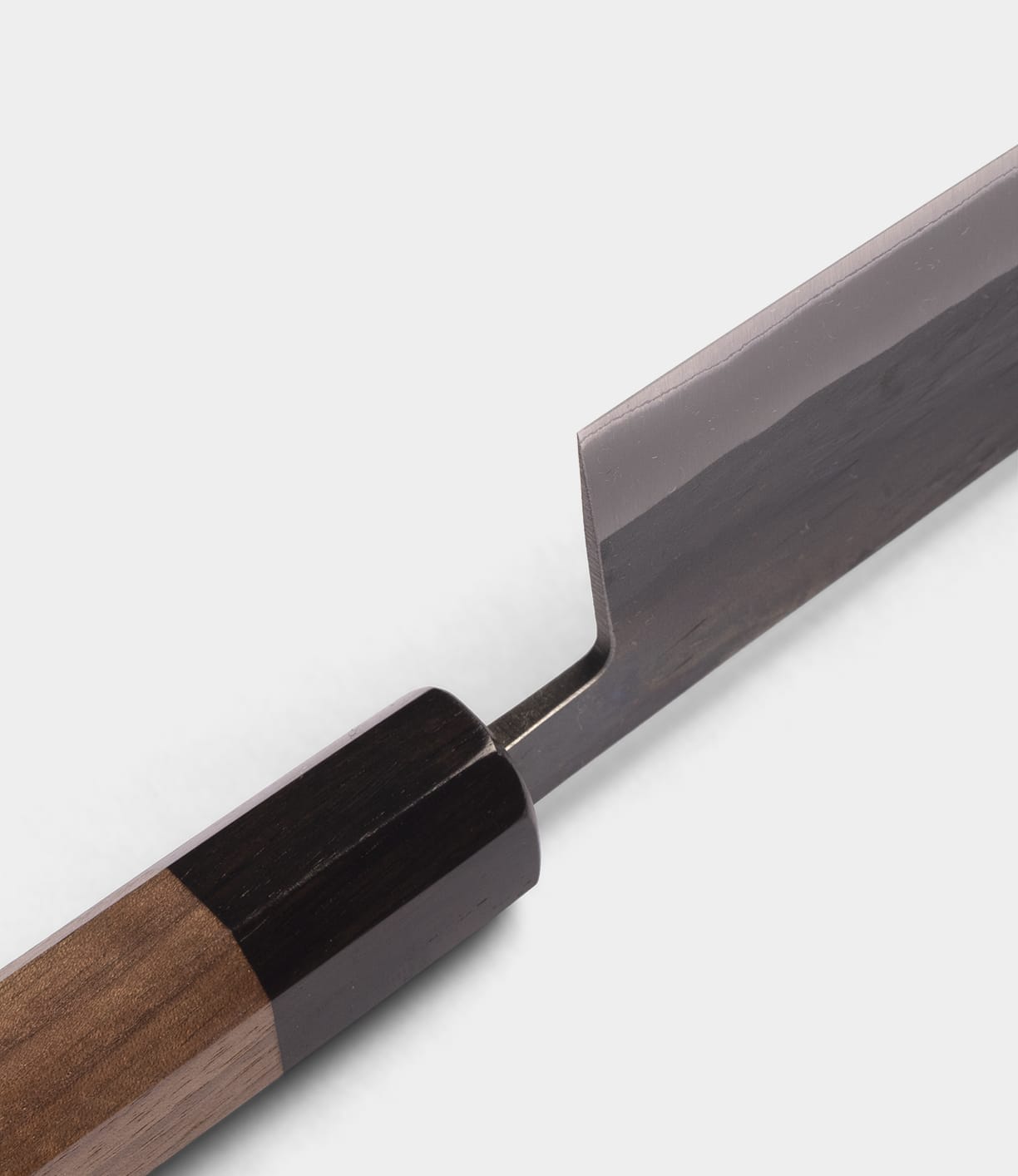 Close-up of the Best Made Co. Aogami Santoku Knife, featuring a wooden handle with a dark bolster and part of its shiny, straight-edged Blue Paper Steel blade, set against a plain light background.