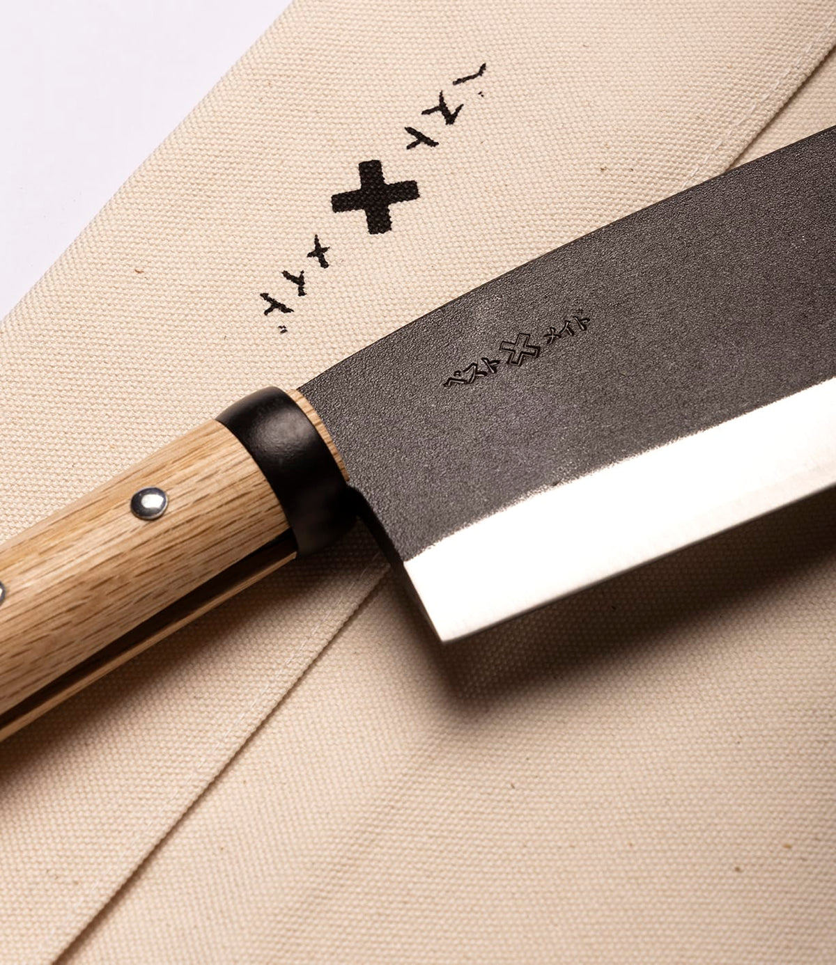 A close-up of the Best Made Co. Azuma Hatchet with a wooden handle rests on a beige cloth, both adorned with minimalist black symbols, capturing the refined craftsmanship inspired by Japanese carbon steel designs.