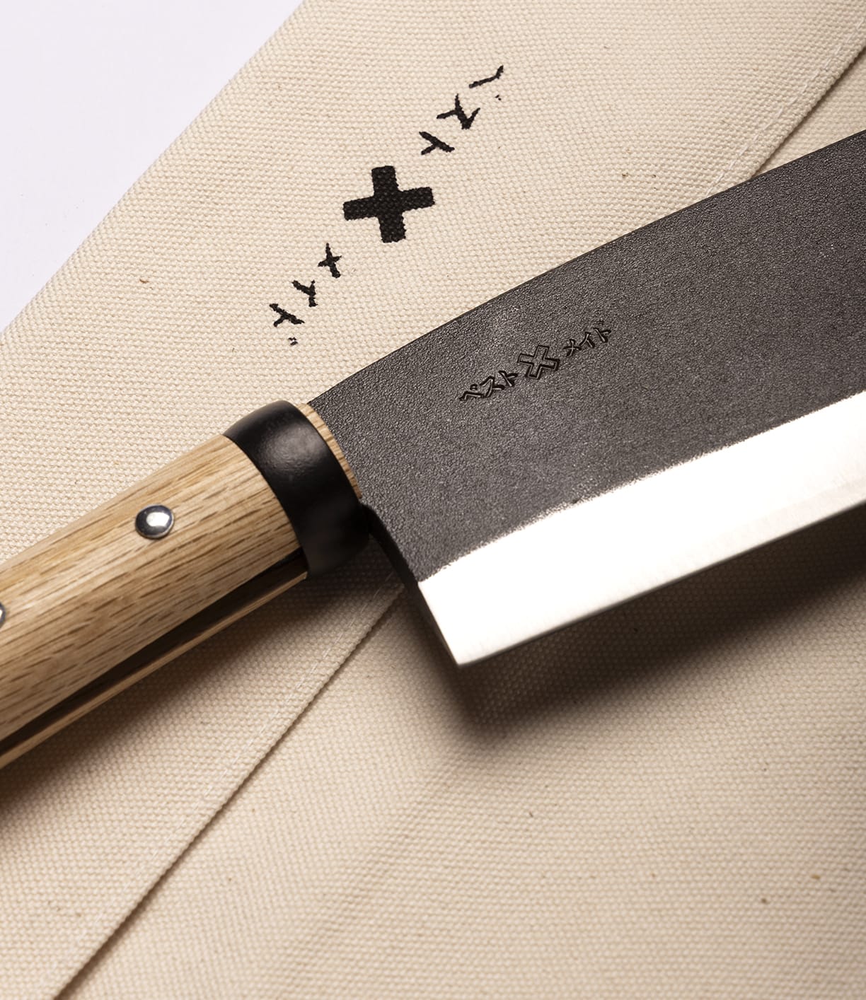 A close-up of the Best Made Co. Azuma Hatchet with a wooden handle rests on a beige cloth, both adorned with minimalist black symbols, capturing the refined craftsmanship inspired by Japanese carbon steel designs.