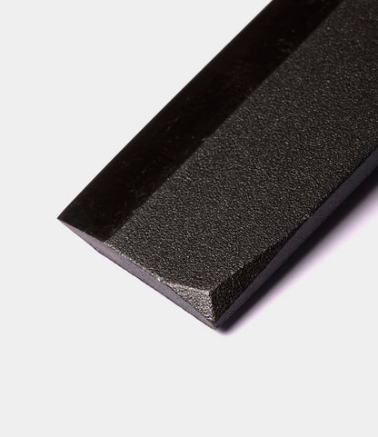 Close-up of the corner of a black, rectangular, textured object with a beveled edge, set against a white background—evoking the refined craftsmanship found in the Sayanata Hatchet by Best Made Co., forged from premium Nippon carbon steel.