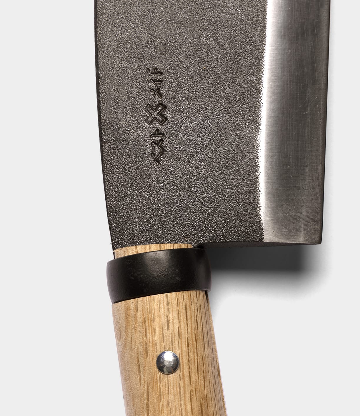 Close-up of the Azuma Hatchet by Best Made Co., showcasing its wooden handle with a metal rivet and an engraved design on the blade near the handle, echoing the traditional style of Japanese carbon steel hatchets, set against a plain light background.