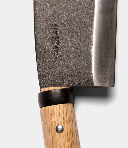 Close-up of the Azuma Hatchet by Best Made Co., showcasing its wooden handle with a metal rivet and an engraved design on the blade near the handle, echoing the traditional style of Japanese carbon steel hatchets, set against a plain light background.