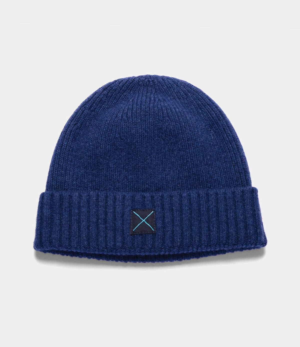 Navy blue lambswool Cap of Courage beanie with a folded cuff and a small square patch featuring a light blue embroidered X.