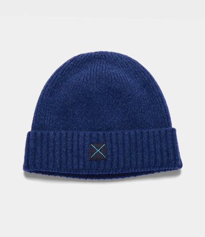 Navy blue lambswool Cap of Courage beanie with a folded cuff and a small square patch featuring a light blue embroidered X.