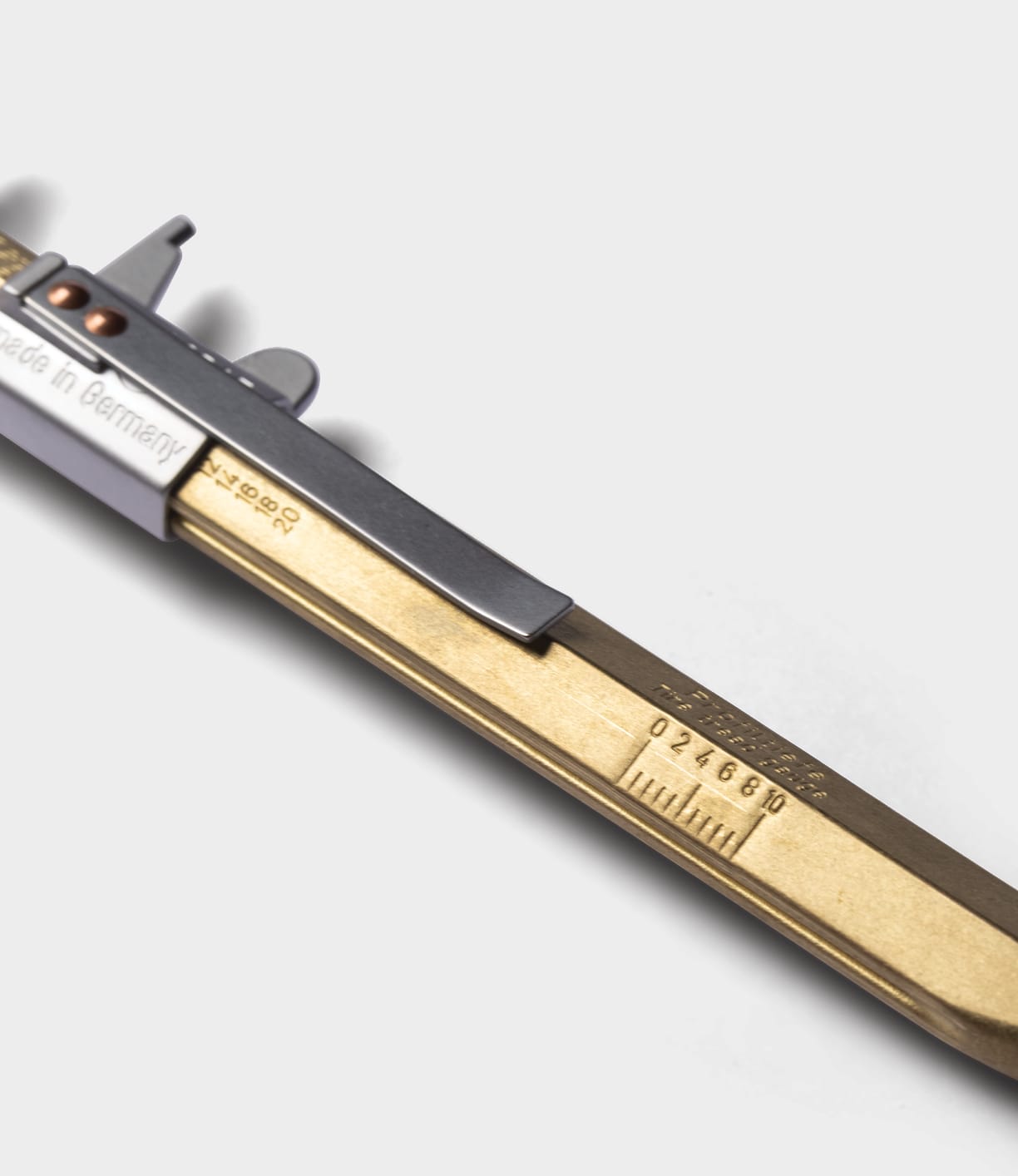 A close-up of a brass and steel slide caliper on a white background, with engraved markings and a serial number—evoking the precision engineering of the Best Made Co. Brass Messograf Pen.