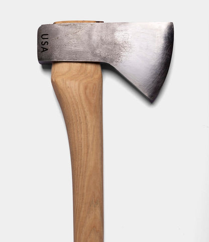 A close-up of The Optimist axe by Best Made Co. features a wooden handle and a 5160 carbon steel blade engraved with "USA," set against a plain white background.