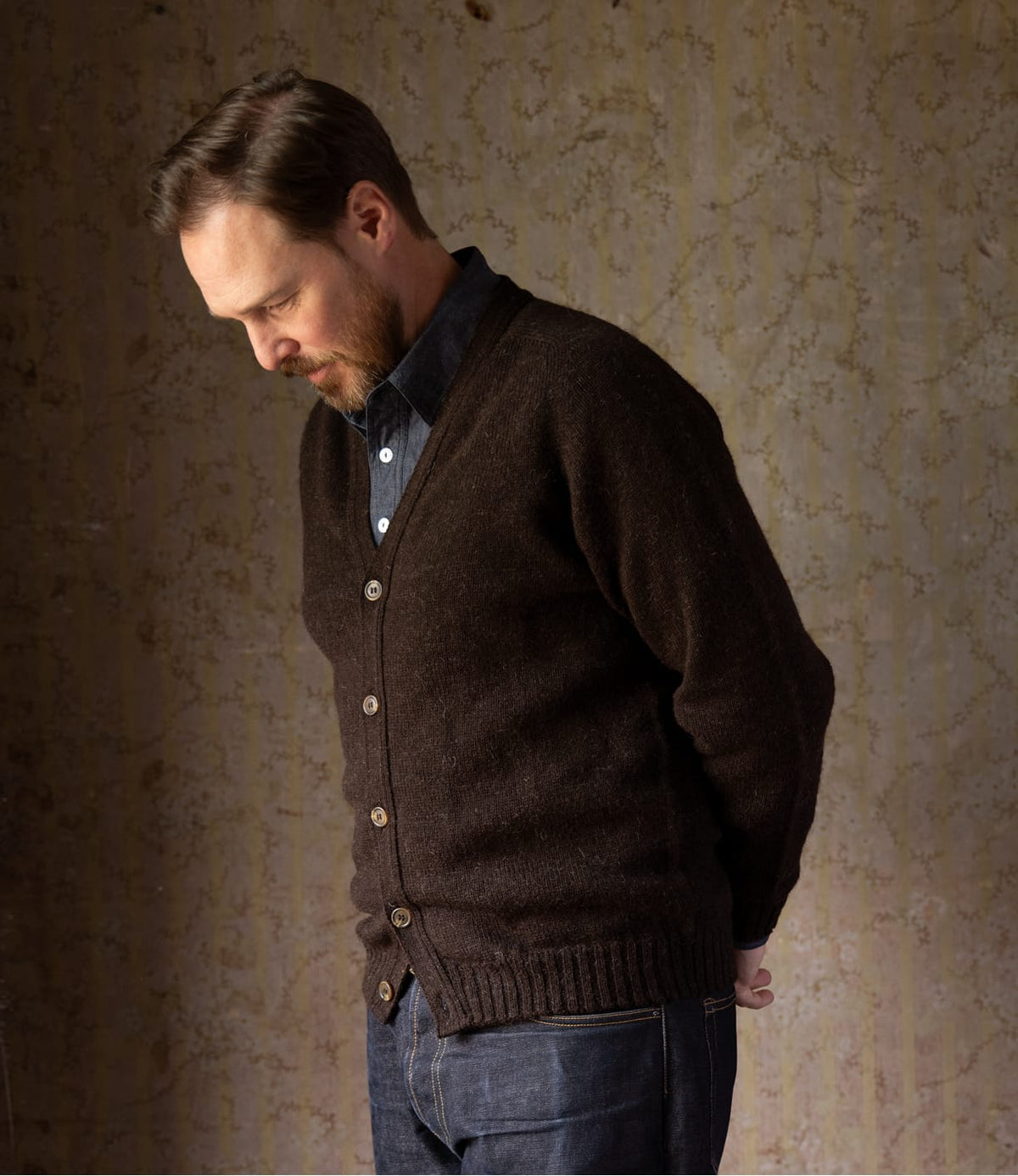 A man wearing a black Shetland wool Black Sheep Cardigan by Best Made Co. over a blue collared shirt.