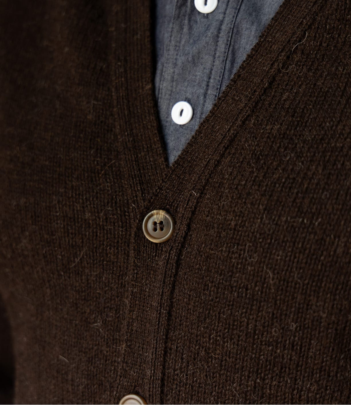 Close-up of a Black Sheep Cardigan by Best Made Co. in black Shetland wool, styled as a V-neck worn over a grey button-down shirt.