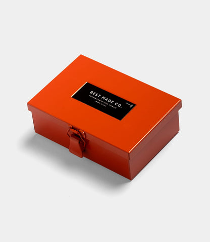 The Type 6 Strongbox Orange by Best Made Co. is a rectangular, orange steel box with a clasp and black lid label, shown on a white background for secure storage.