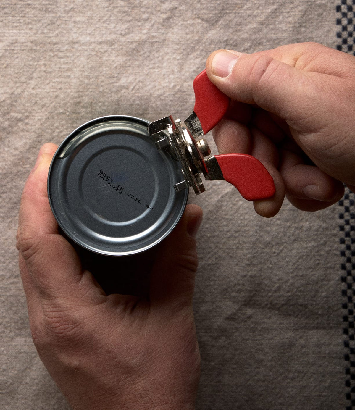 Hands using a compact Nogent French Can Opener to open a metal tin.