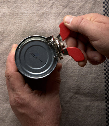 Hands using a compact Nogent French Can Opener to open a metal tin.