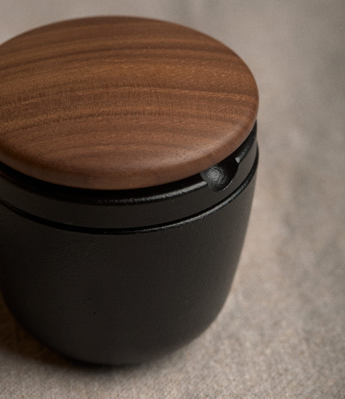 A small, black Best Made Co. Cast Iron Grinder with a round walnut lid.