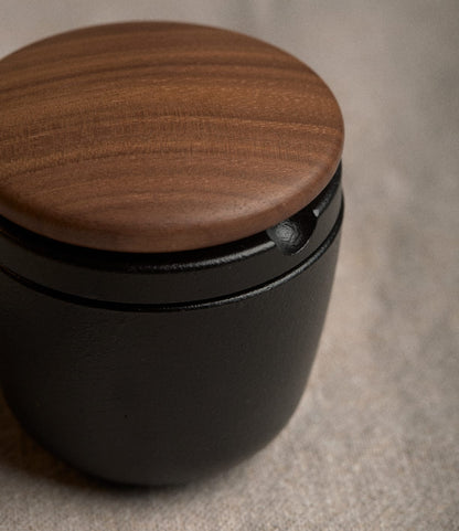 A small, black Best Made Co. Cast Iron Grinder with a round walnut lid.