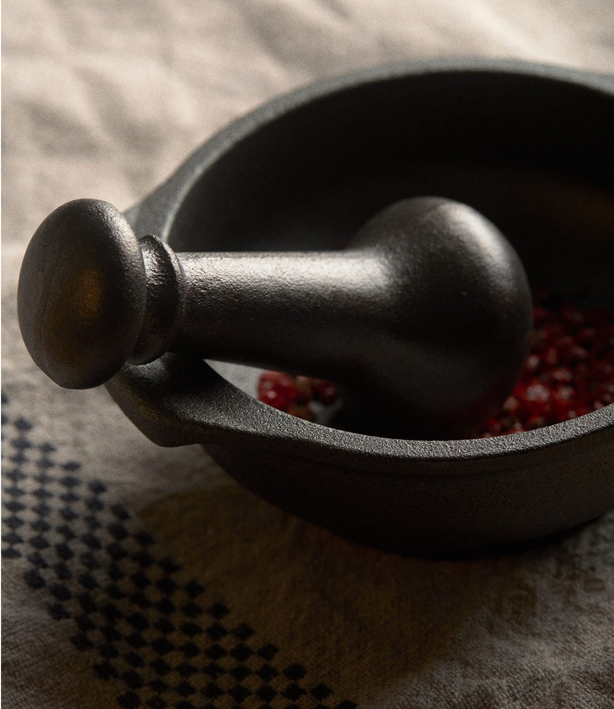 A black cast iron Cast Iron Mortar and Pestle by Skeppshult containing red peppercorns.