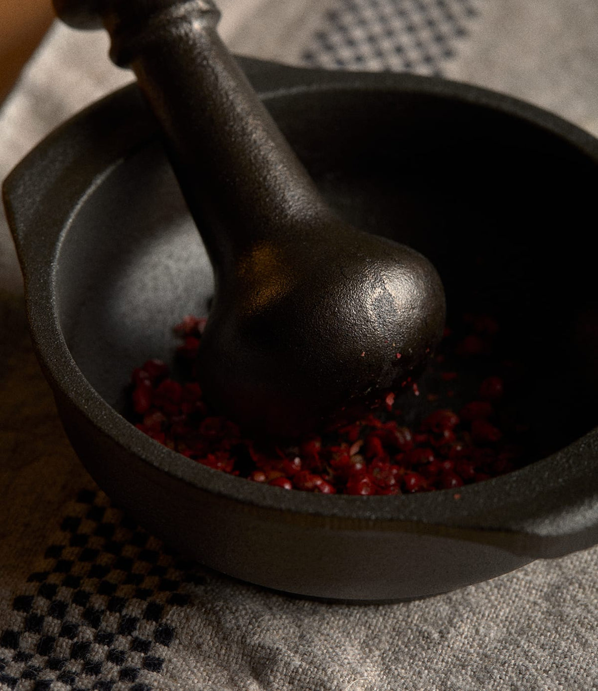 A black Best Made Co. Cast Iron Mortar and Pestle grinding red peppercorns.
