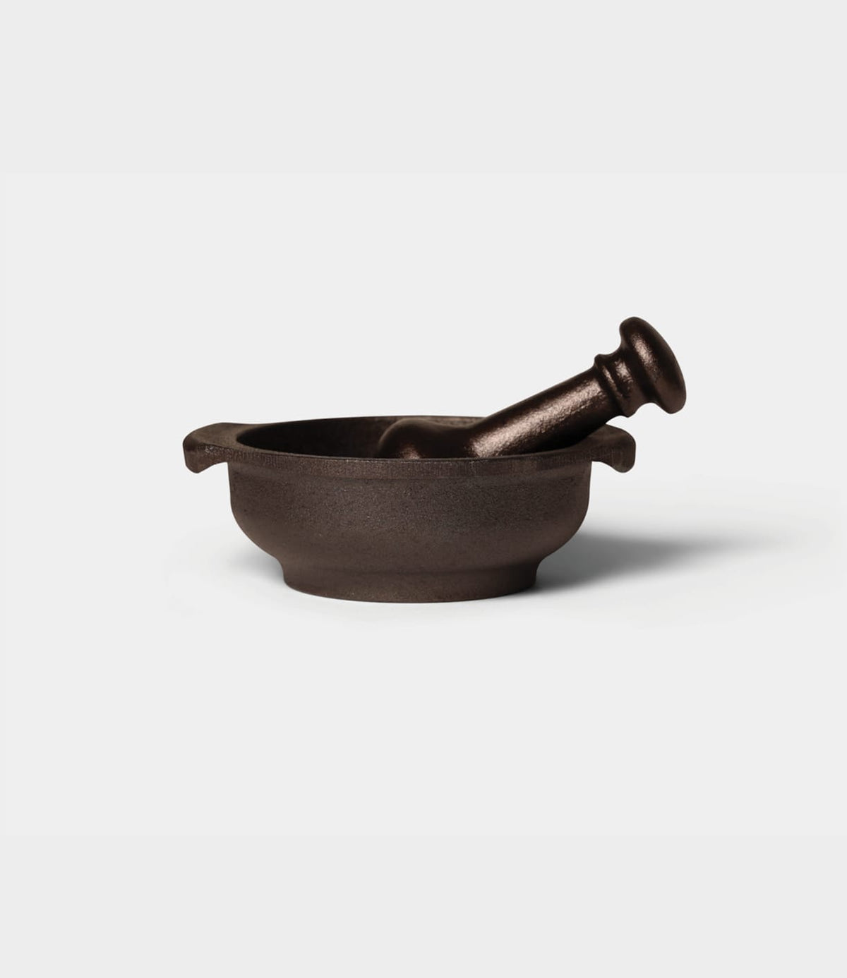 A Best Made Co. Cast Iron Mortar and Pestle with two side handles and a matching pestle resting inside the traditional kitchen grinding tool.