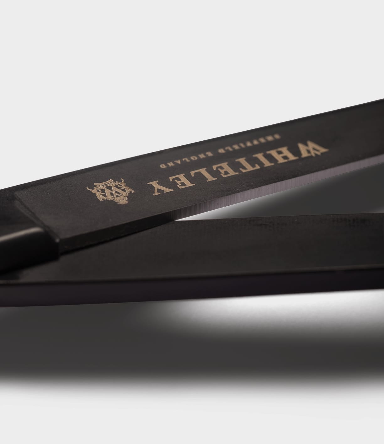 Close-up of Best Made Co. Ten-Inch Paper Scissors with black handles and gold branding on the blade, crafted from hot-forged carbon steel, set against a plain light gray background.