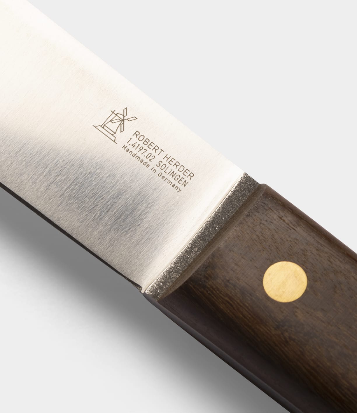 A close-up of the Best Made Co. Sailor’s Knife featuring a Brazilian Teak handle with a brass rivet. The Niolox steel blade is engraved with a windmill logo and the text: ROBERT HERDER, 1872 SOLINGEN, Handmade in Germany.