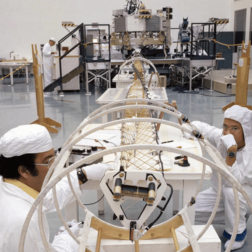 Two scientists in lab coats working on a large mechanical structure in a laboratory.
