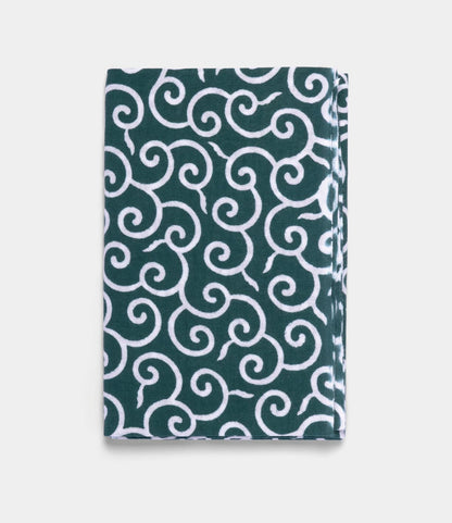 A folded Karakusa Tenugui by Best Made Co.—a hand-dyed Japanese cloth with a dark green background and intricate white swirling pattern—displayed on a plain light gray surface.