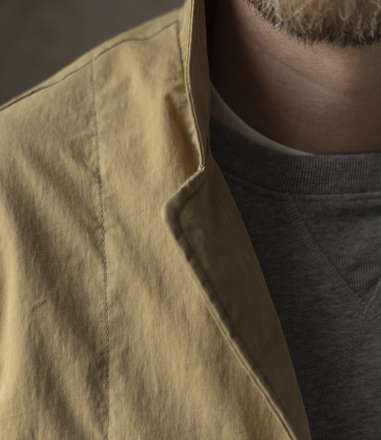 Close-up of a person wearing the Best Made Co. Possibilities Jacket Tan over a grey crew-neck sweatshirt, with part of their lower face and beard visible, highlighting the jacket's texture and layered look.
