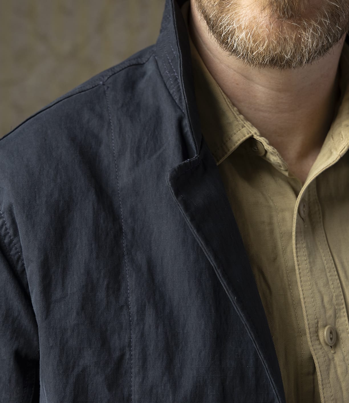 Close-up of a man wearing the Best Made Co. Possibilities Jacket Navy over a beige button-up shirt, collar turned up. Only his light brown beard and part of his upper body are visible.