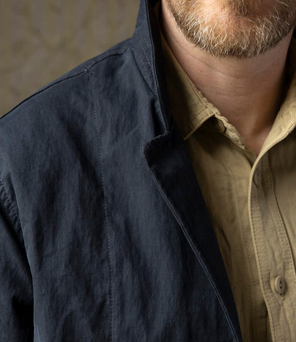 Close-up of a man wearing the Best Made Co. Possibilities Jacket Navy over a beige button-up shirt, collar turned up. Only his light brown beard and part of his upper body are visible.