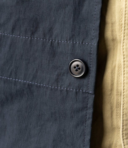 Close-up of the Possibilities Jacket Navy by Best Made Co., made from dark blue cotton Cordura with a black button and stitched seam, shown beside tan textured fabric.