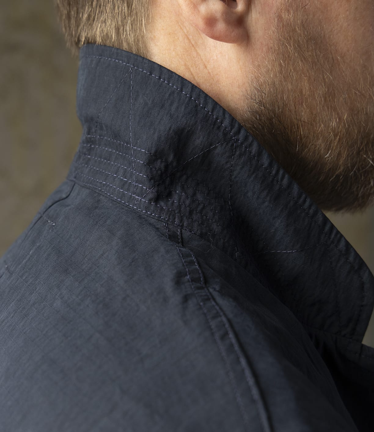 Close-up of a man's neck and jaw with a short beard, wearing the Best Made Co. Possibilities Jacket Navy—crafted from durable cotton Cordura with detailed stitching and textured fabric near the collar for versatile lightweight style.
