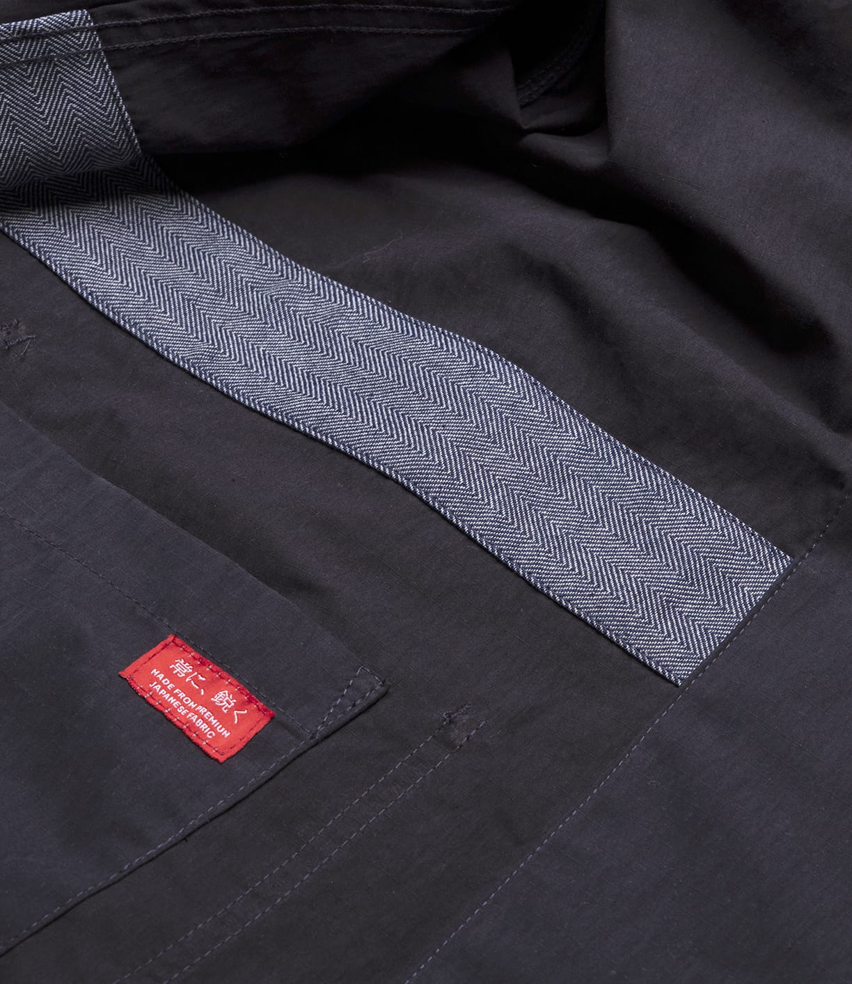 Close-up of the inside of the Best Made Co. Possibilities Jacket Navy, featuring herringbone-patterned trim and a red label with white text stitched onto an interior pocket.