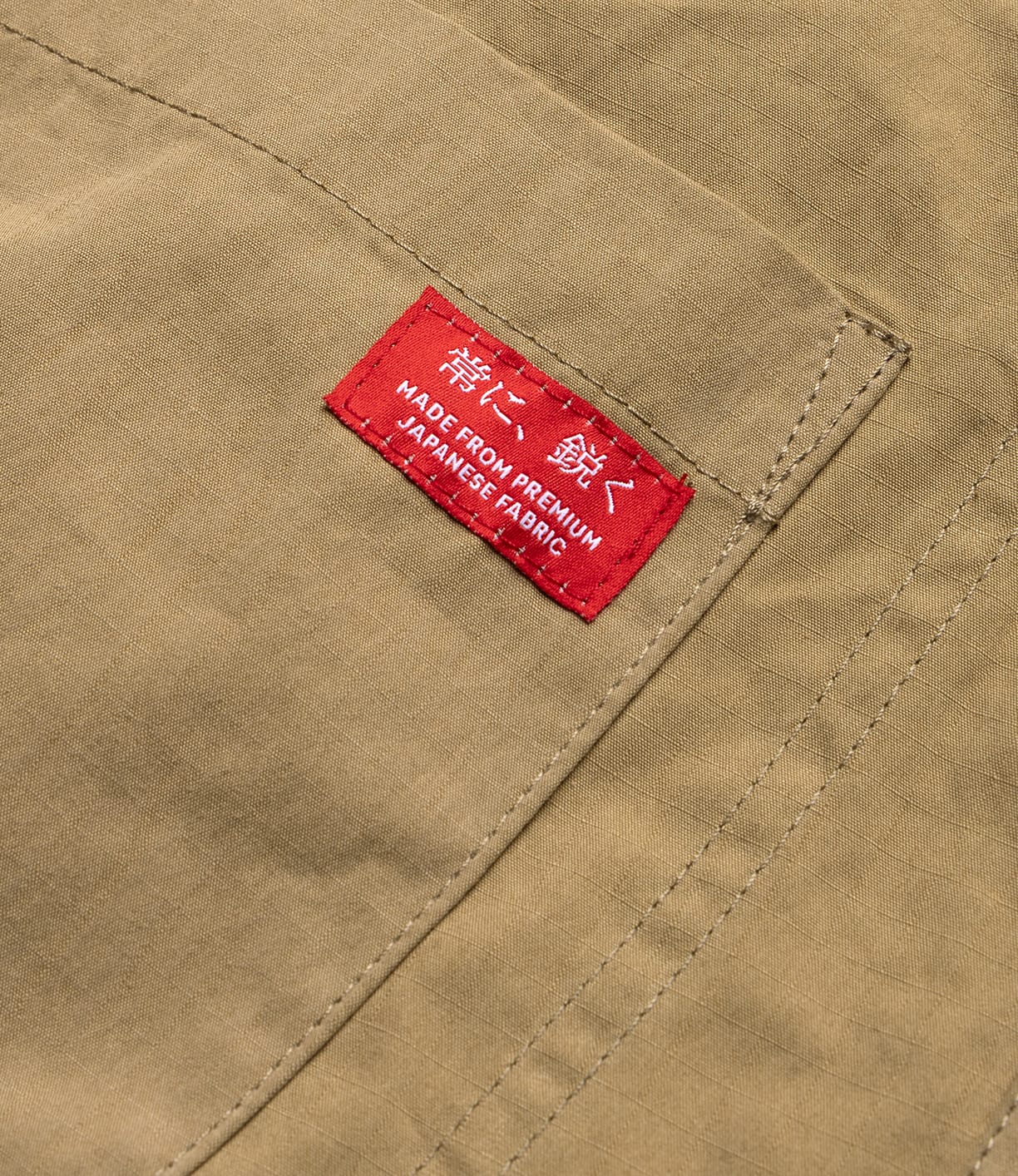 Close-up of tan fabric with visible stitching and a red label reading "MADE FROM PREMIUM JAPANESE FABRIC"—showing the quality detailing on the Best Made Co. Possibilities Jacket Tan, crafted for durable lightweight outerwear.