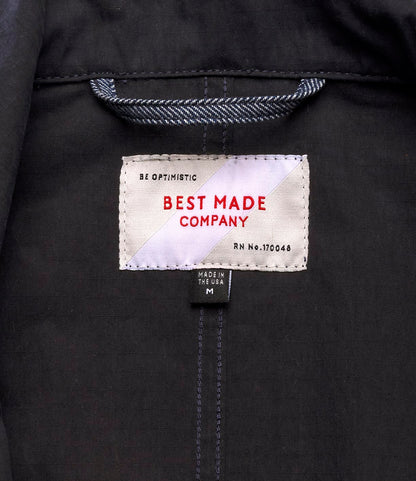 A close-up of the Possibilities Jacket Navy label shows "BE OPTIMISTIC" and "Best Made Co." in red, with size M and "MADE IN THE USA" printed on a smaller black tag below.