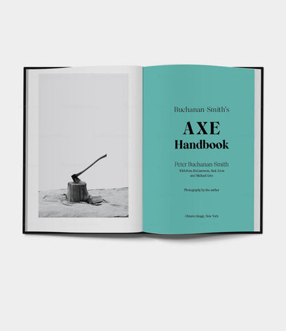 An open book shows a black-and-white photo of an axe in a stump. The right page displays Buchanan-Smith’s Axe Handbook (signed) by Best Made Co., with title and author details in black and teal text.