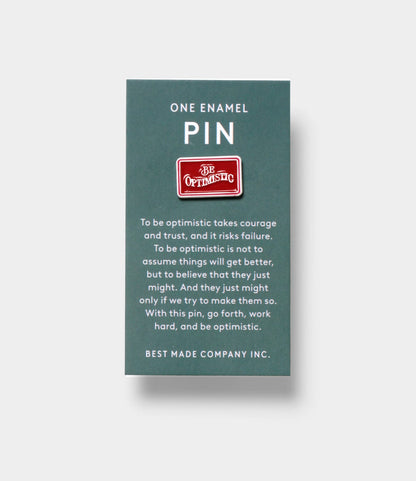 The Be Optimistic Pin by Best Made Co. is a red enamel pin with “Be Optimistic” on it, attached to a card featuring an inspirational optimism quote—an uplifting accessory to boost your mindset.