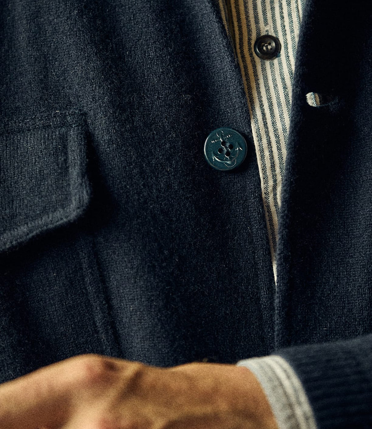 Close-up of a dark navy Knit Lambswool CPO with anchor-embossed buttons, worn over a striped button-down shirt.