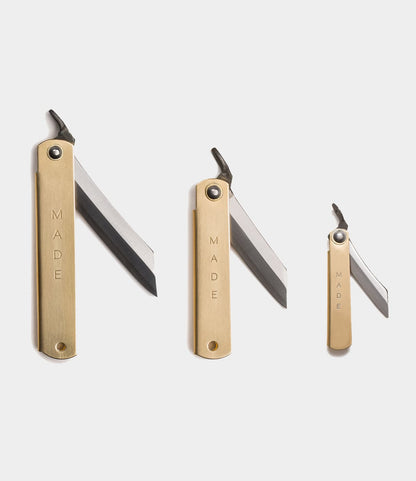 Three Max Brass Higo Knives by Best Made Co., in small, medium, and large sizes, are shown with partially opened silver blades. Their brass handles are engraved with MADE, highlighting this classic Japanese folding knife design.