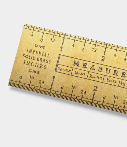 A close-up of the Best Made Co. Measure Twice 12 inch Solid Brass Ruler, featuring precision-engraved inch and fraction markings—16THS, 32NDS, IMPERIAL SOLID BRASS INCHES—along its top and bottom edges.