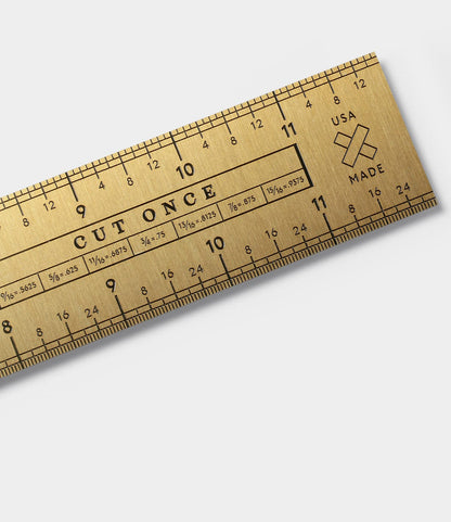 A close-up of the Best Made Co. Measure Twice 12 inch Solid Brass Ruler featuring precision markings, “CUT ONCE” engraved in the center, and a USA MADE label with a small crossed bandage icon on the right.