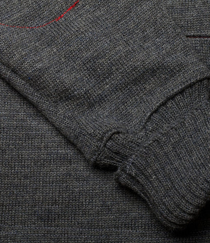 A close-up of the Best Made Co. Dehen Shawl Neck Sweater Charcoal sleeve laid across the body, featuring a red stitch near the top—a rugged sweater crafted in Portland, Oregon.