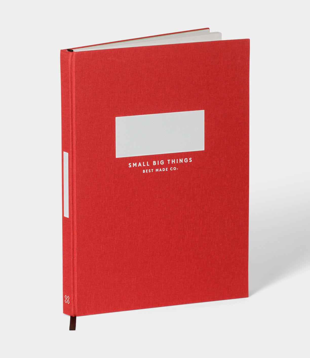 The S.B.T. Max Cloth-Bound Notebook by Best Made Co., in red with a blank label, stands upright against a plain light gray background. “SMALL BIG THINGS BEST MADE CO.” is printed in white on the cover.