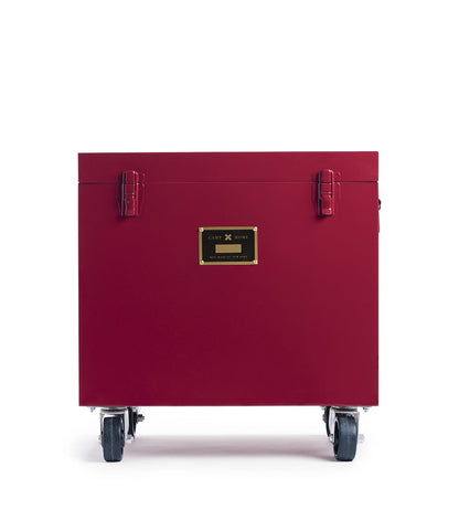 A red, rectangular Rolling Footlocker by Best Made Company Archive, constructed from 22-gauge steel with metal latches and a gold label, is set on four caster wheels and photographed against a plain white background.